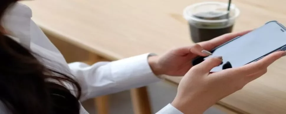 A woman sitting at a table, focused on her cell phone, with a relaxed expression on her face.
