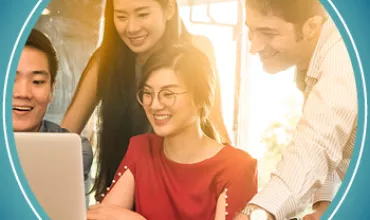 A group of people happily gathered around a laptop in sunlight.