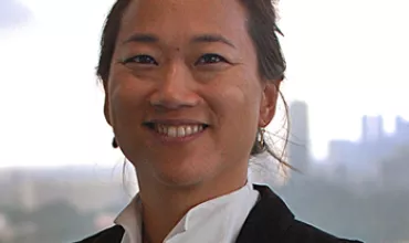 Person smiling in a professional setting with a cityscape in the background.