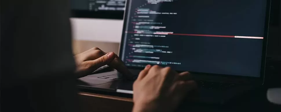 Hands typing code on a laptop in a dark room
