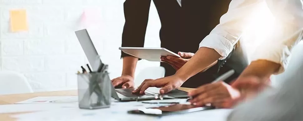 Three people working at a desk with laptops and a tablet.