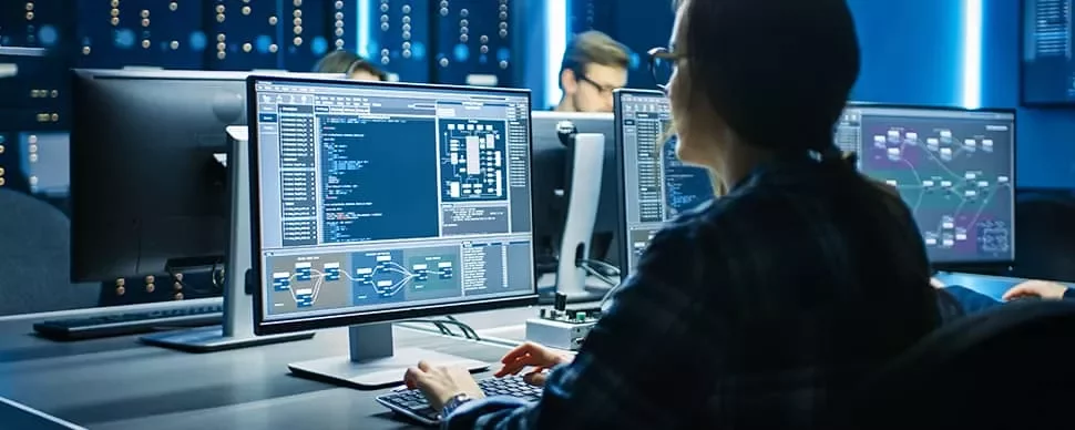 Person working at a desk with computer screens displaying code and diagrams.