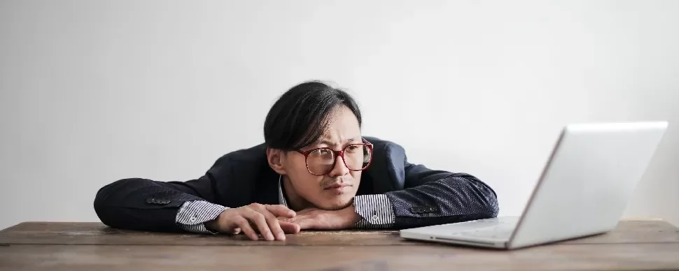 A person leaning on a desk, looking at a laptop.