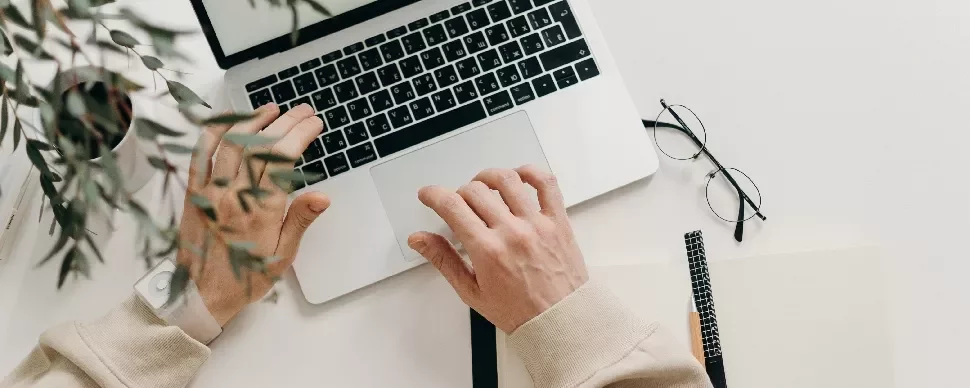 Person typing on a laptop with glasses and notebook nearby