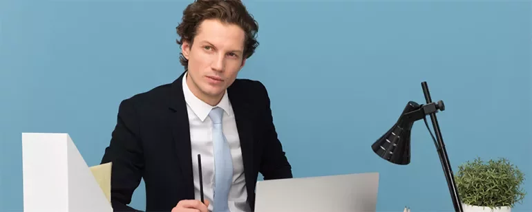 Professional sitting at a desk with a laptop and lamp.