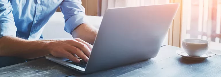 Person typing on a laptop with a cup of coffee on the table.