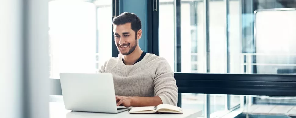 A person smiling while looking at a laptop on a table.