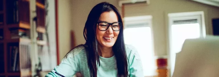 Person smiling while using a computer in a room with bookshelves.