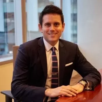 Person in suit smiling at a desk in an office.