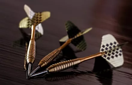 Three darts lying on a table, blurred background.