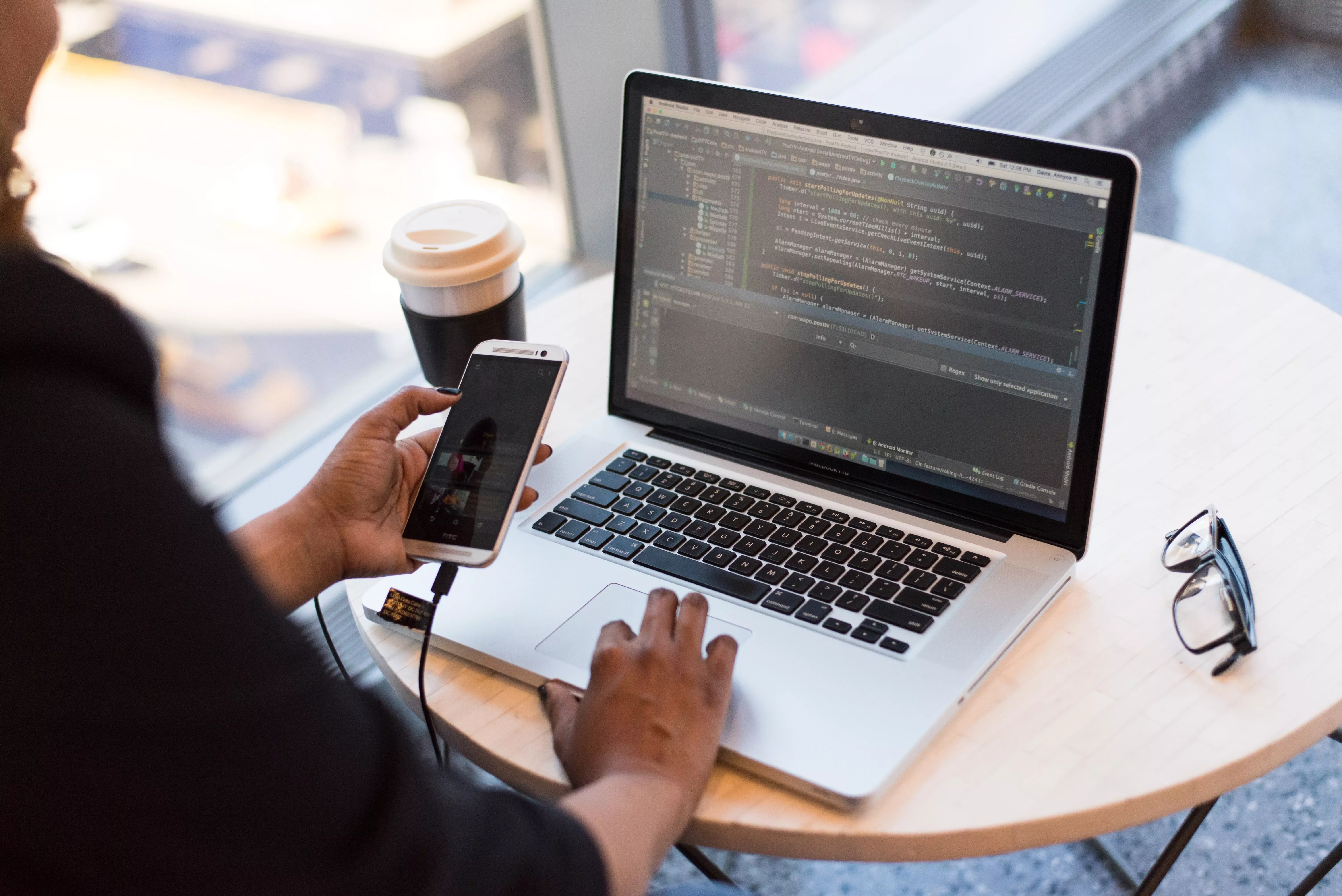 A software developer working on a laptop with a smartphone on a table by the window.