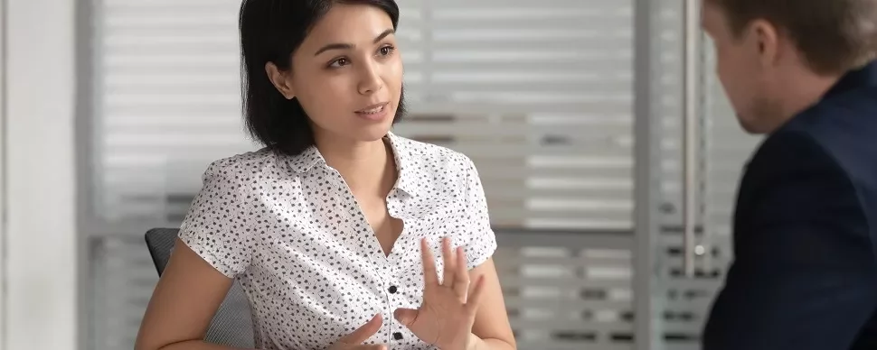 Two people in an office setting, one person in a light shirt is speaking.