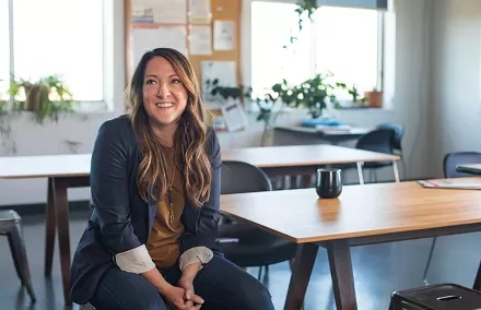 Person smiling while sitting at a desk in an office with plants.