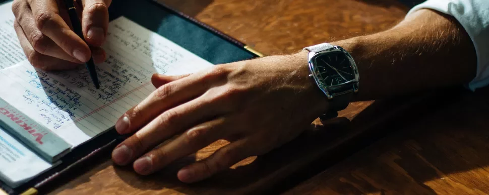 A hand wearing a watch writing on a notepad.