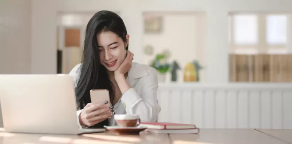 一個人在桌前使用智慧手機和筆記本電腦，微笑著看屏幕。