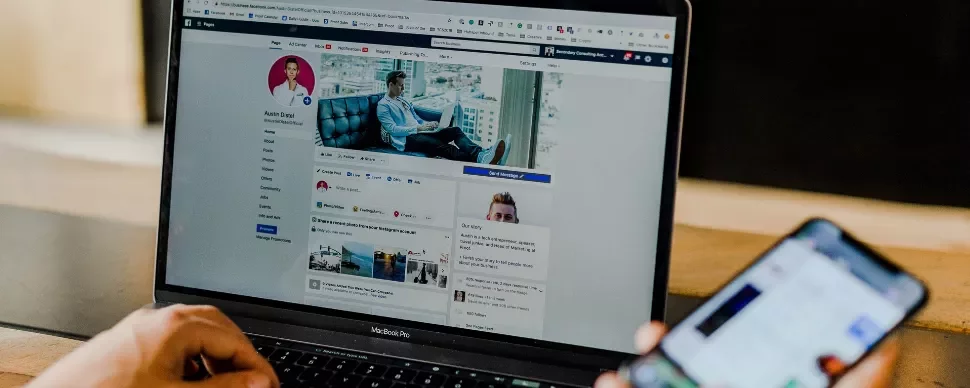 Laptop open to a social media profile next to a hand holding a smartphone.