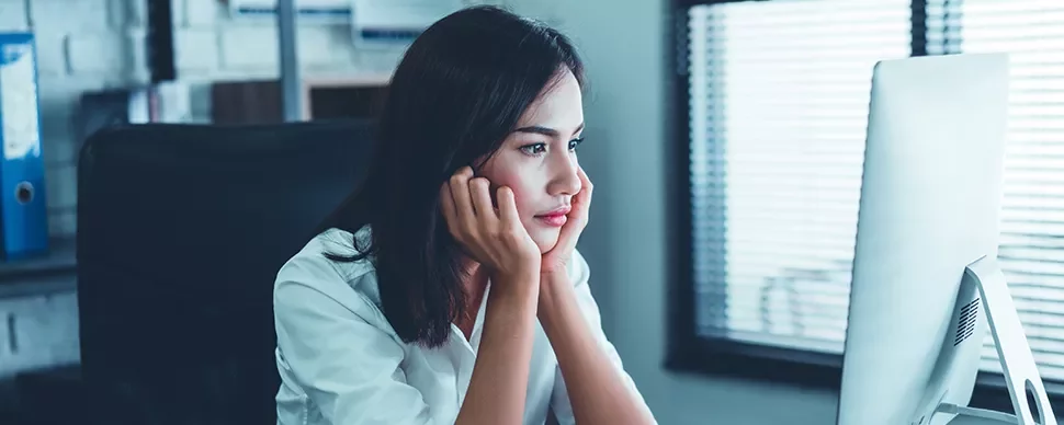 Person sitting at a desk looking thoughtfully at a computer screen.