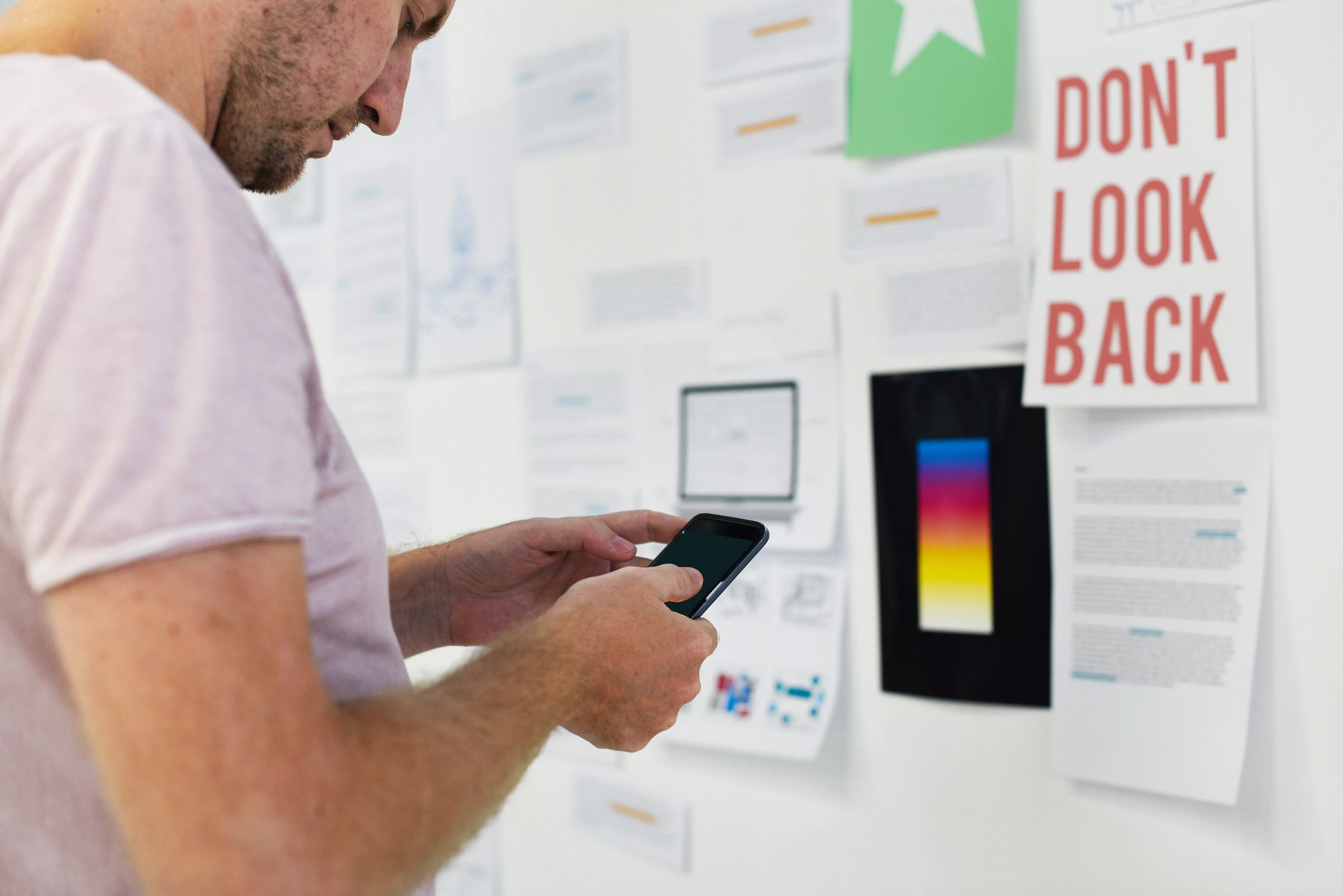 A person using a smartphone while examining notes on a wall.