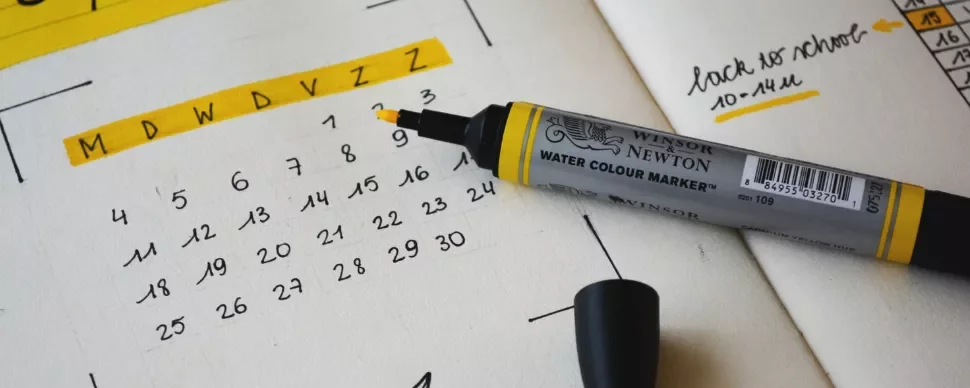 Yellow marker on a planner next to a calendar showing dates with notes.