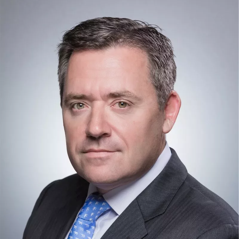 Close-up portrait of a person in a suit with a light gray background.