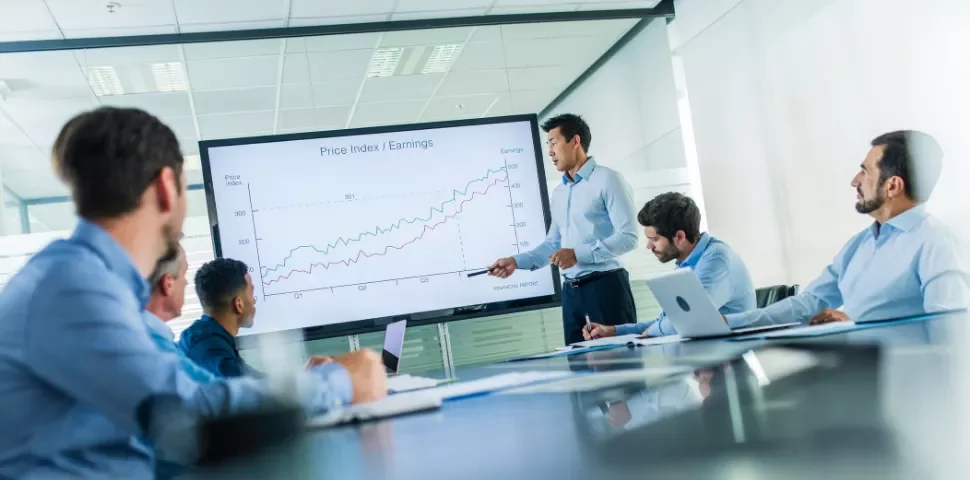 A meeting with a speaker presenting a chart, while others listen.