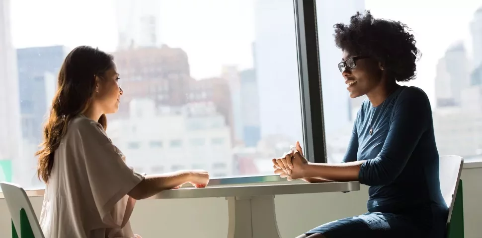 Two people talking at a table in a brightly lit room.
