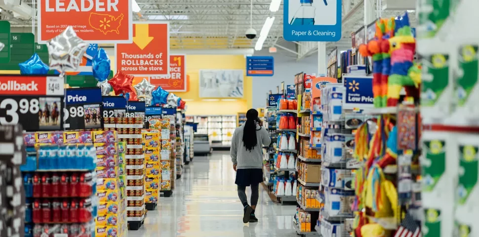 Customer walking down a grocery store aisle with shelves full of products.